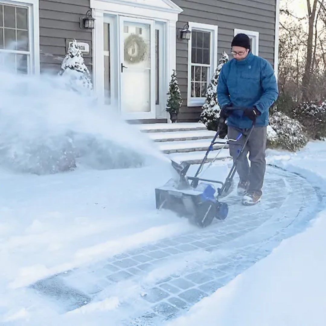 A blue and black-framed snow blower in action, clearing snow from a pathway.